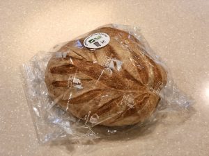 A rustic, round sourdough loaf wrapped in transparent compostable film from orfix